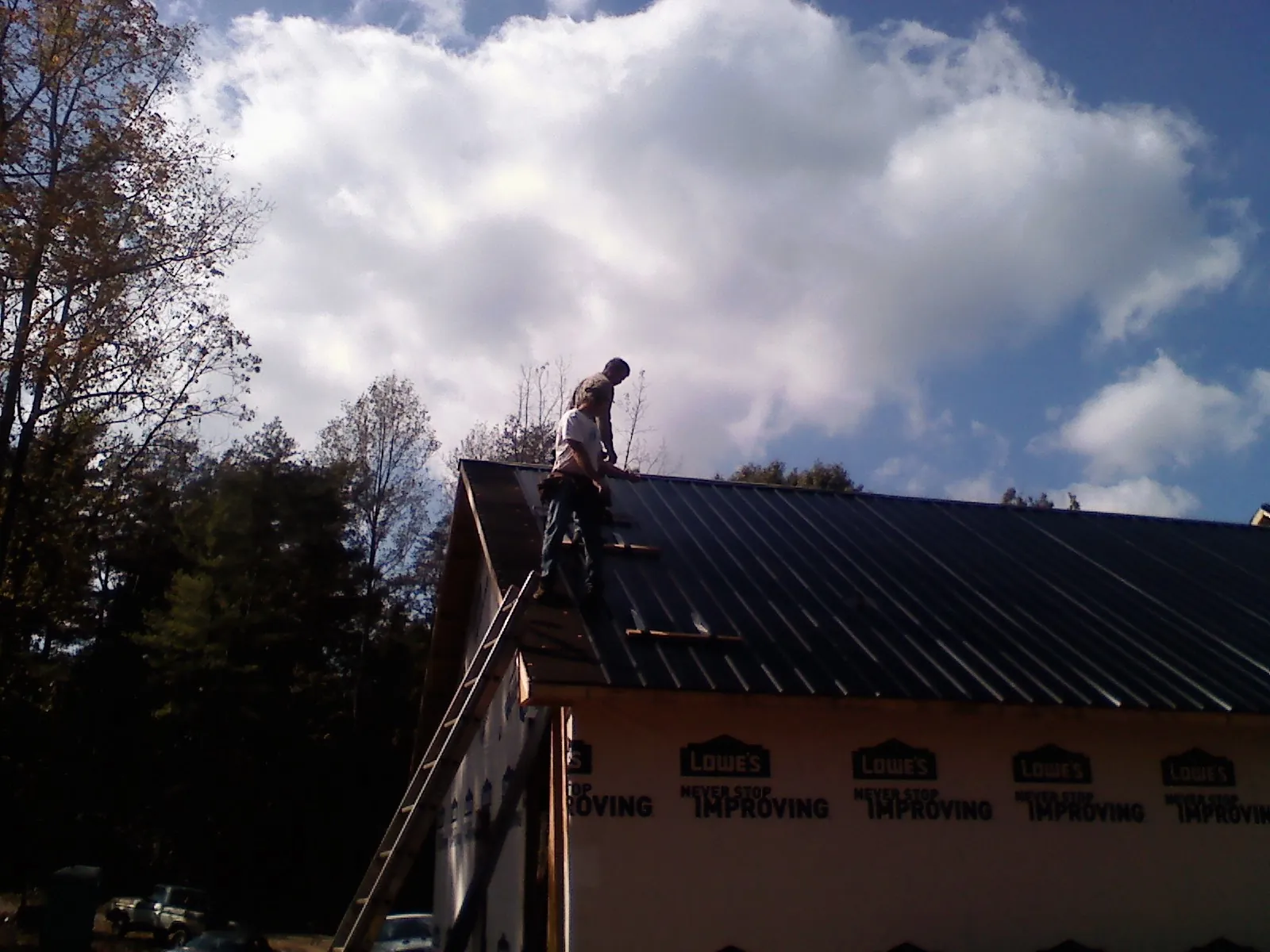 Roofer fastening dark metal panels high against a cloudy sky, from a Roof Inspection job in Chester