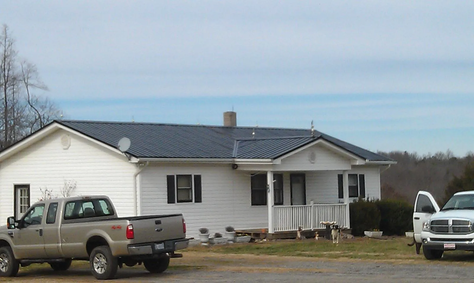 Finished dark metal roof on a white ranch home with work trucks parked in Chester